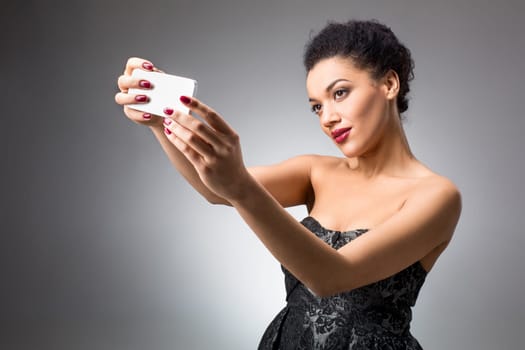 Portrait of a Beautiful brunette doing selfie in a black dress on a light background