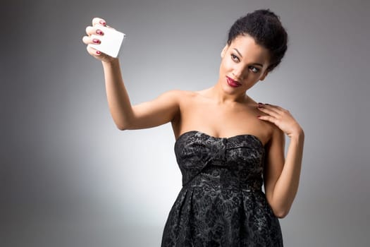 Portrait of a Beautiful brunette doing selfie in a black dress on a light background