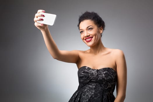 Portrait of a Beautiful brunette doing selfie in a black dress on a light background