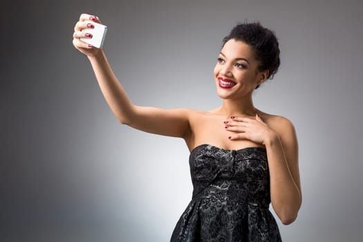 Portrait of a Beautiful brunette doing selfie in a black dress on a light background