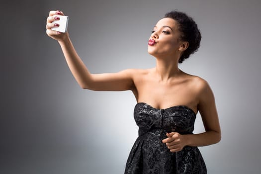 Portrait of a Beautiful brunette doing selfie in a black dress on a light background