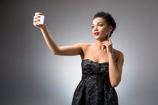 Portrait of a Beautiful brunette doing selfie in a black dress on a light background