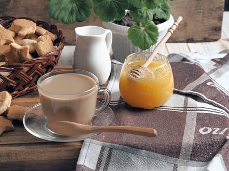 Food background.Healthy homemade food.A cup of tea with milk and homemade butter cookies. Still life on a brown background of a rustic kitchen table with scattered biscuits and honey.