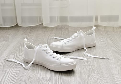 White sneakers with untied laces are on the floor