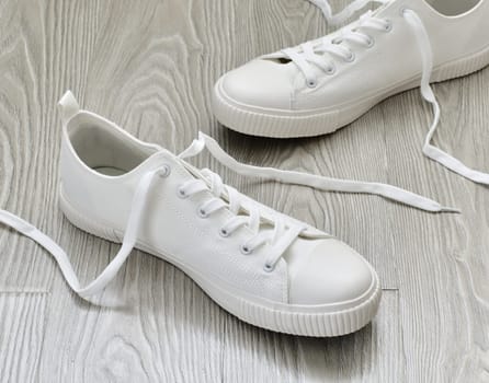 White sneakers with untied laces are on the floor