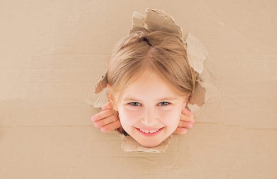 Smiling little girl peeping from hole in cardboard box