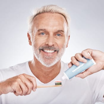 Toothbrush, face and senior man with toothpaste in studio on a gray background. Portrait, cleaning and elderly male model holding product for brushing teeth, dental wellness and healthy gum hygiene
