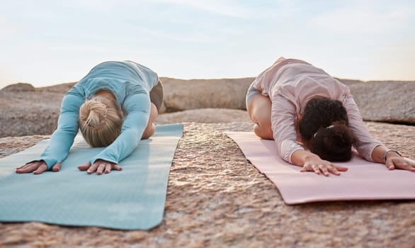 Yoga, women or childs pose on beach mat in workout, training or bonding exercise for back pain. Relax, stretching or yogi friends in nature pilates, fitness flexibility or healthcare wellness on rock.