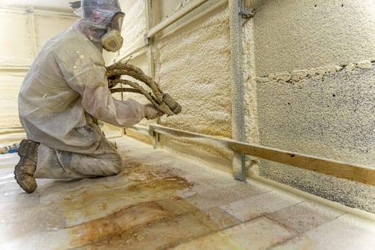 A worker in a protective suit insulates the walls of the basement of the house with polyurethane foam spraying it from a nozzle. filling the walls with foam insulation. Energy saving, warm modern house. modern technologies