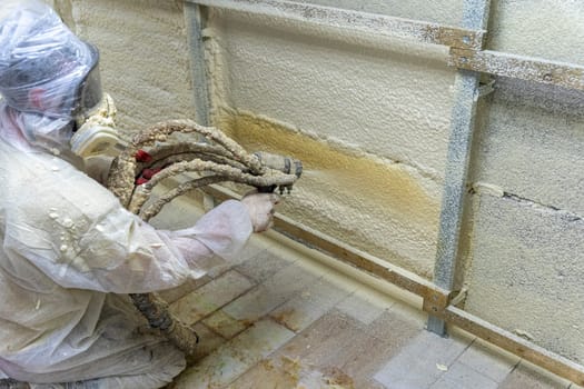 A worker in a protective suit insulates the walls of the basement of the house with polyurethane foam spraying it from a nozzle. filling the walls with foam insulation. Energy saving, warm modern house. modern technologies