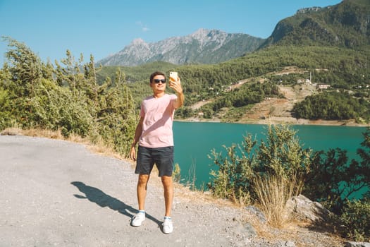 Man taking selfie on mobile phone of mountains lake background. Traveler male having video chat on cellphone on the blue lake outdoors travel adventure vacation.