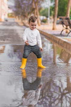 boy in yellow rubber boots jumping over a puddle in the rain.