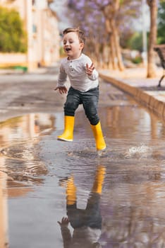 boy in yellow rubber boots jumping over a puddle in the rain.