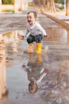 boy in yellow rubber boots jumping over a puddle in the rain.