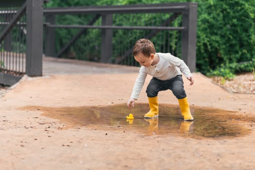 happy child with yellow rubber duck in a puddle in autumn in nature.