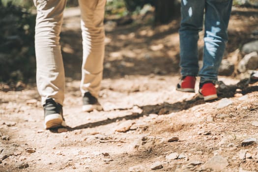 Close-up rear view of tourists heels school boy and his dad walking a stone footpath in spring forest. Child boy and father wearing casual clothes while hiking in summer greenwood forest.