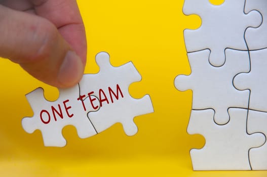 Hand holding missing jigsaw puzzle with One Team text. Teamwork concept.