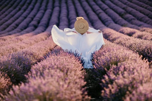 Happy woman in a white dress and straw hat strolling through a lavender field at sunrise, taking in the tranquil atmosphere