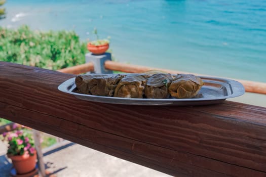 A dish with served dolmades, wrapped in little rolls, a traditional dish with stuffed vine leaves, against a defocused seafront background.