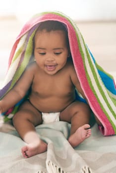 African baby, girl and sitting for smile with blanket, young or healthy in bedroom at family home. Black infant, toddler and bed with towel for growth, care and health in morning sunshine at house.