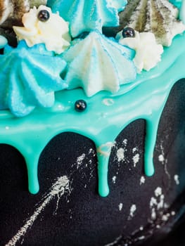 frosted black painted cup cake with blue turquoise dripping and colored handmade meringue topping studio white isolated background