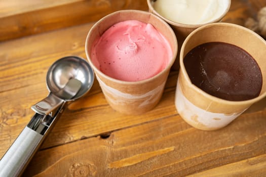 Ice cream in a box with different flavors stand on a wooden tray along with a metal ice cream scoop