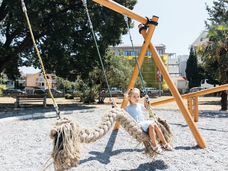 Little girl swings on a swing in the form of a braid on the playground. High quality photo