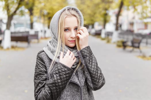 A young blonde walks through the autumn city in a gray coat. The concept of urban style and lifestyle