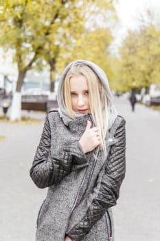 A young blonde walks through the autumn city in a gray coat. The concept of urban style and lifestyle