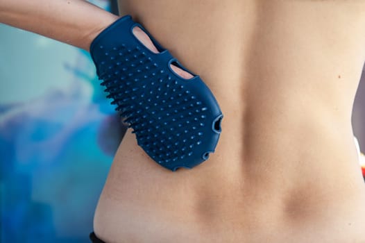 Anticellulite silicone or rubber massager - mitten for body in female hand on body background.