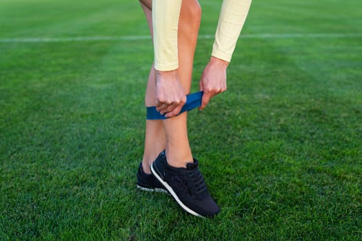 A girl in sneakers starts putting on a sports elastic band at the stadium for sports exercises. Sports and health concept