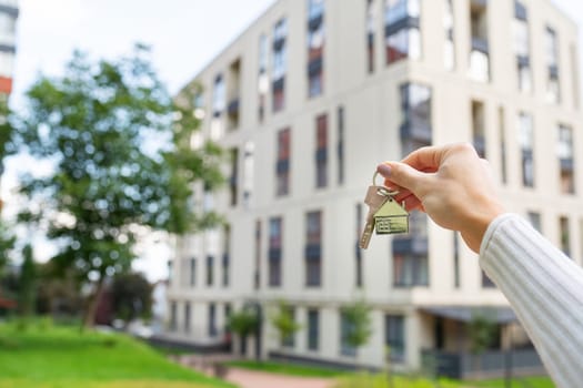 Hand holding keys on the background of a new building, construction concept. Buying real estate, housing, apartments
