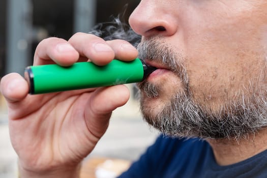 Habit concept, a man smokes an electronic cigarette. Hipster man holding a vaping device. Health safety and addiction. vapor inhalation