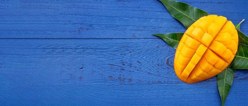 Fresh mango - beautiful chopped fruit with green leaves on dark blue timber background. Tropical fruit design concept. Flat lay. Top view. Copy space