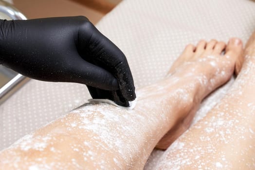 Beautician getting ready to wax female legs in spa center