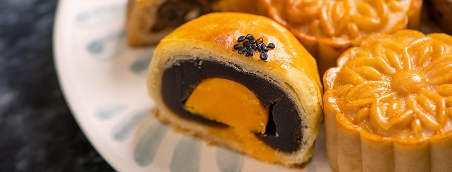 Tasty baked egg yolk pastry moon cake for Mid-Autumn Festival on black slate dark background. Chinese festive food concept, close up, copy space.