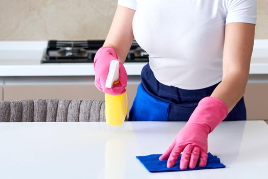 Woman wearing rubber gloves cleaning table with cloth. Disinfecting a kitchen table with bleach