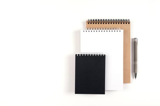 Three blank notepads on a spiral stacked in a stack on a white background. Notebooks with white, black and recycled sheets and pen. Education, office.