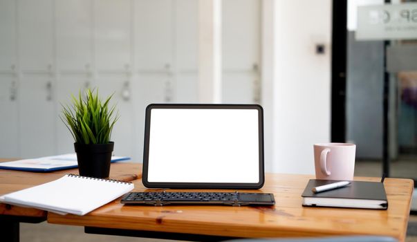 Shot of digital tablet with blank white screen, keyboard, cup of coffee on workspace desk.