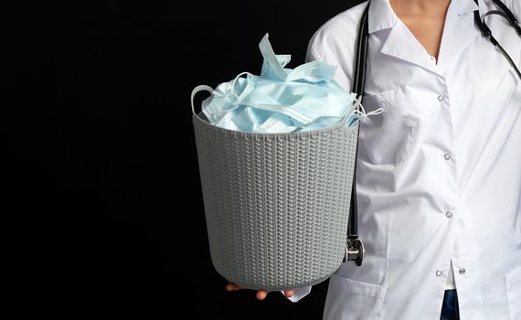 Doctor holding bucket full of used facial masks, virus fight concept with garbage bin