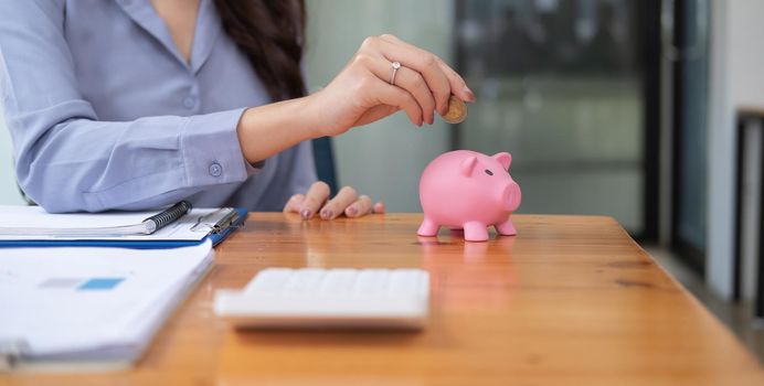 Close up hand of woman putting money coin into pink piggy bank for saving money wealth and financial concept.