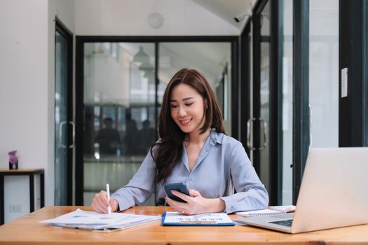 Business asian woman using smartphone for do math finance on wooden desk in office, tax, accounting, financial concept.