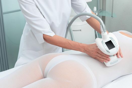 Woman in special white suit getting anti cellulite massage in a spa salon. LPG, and body contouring treatment in clinic