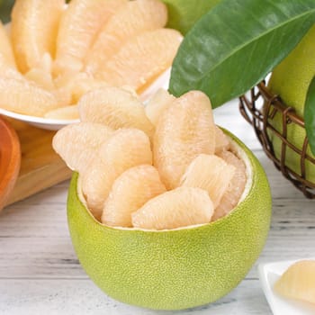 Fresh peeled pomelo, grapefruit, shaddock with green leaf on bright wooden plank table. Seasonal fruit near mid-autumn festival, close up, copy space