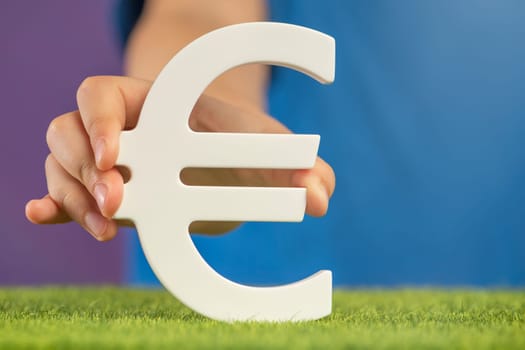 Recession or crisis in Europe. The concept of growth or fall of the economy in Europe. Euro sign in hand on a purple background. High quality photo