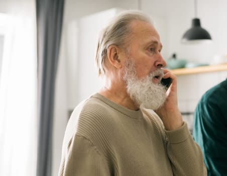 Happy bearded aged senior man talking by phone at home - active senior aged and communication