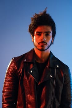 Portrait of a stylish man with curly hair on a blue background multinational, colored light, black leather jacket trend, modern concept. High quality photo