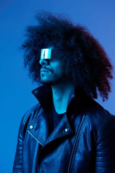 Portrait of fashion man with curly hair with stylish glasses on blue background multinational, colored light, black leather jacket trend, modern concept. High quality photo