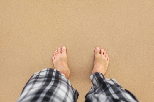 Top down view, man wearing black and white shorts feet in wet sand on beach. Space for text upper part.