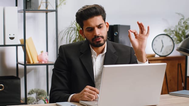 Indian businessman working on laptop computer at home office desk talk on online communication video call with employee, boss. Manager man freelancer support services looking at webcam of computer